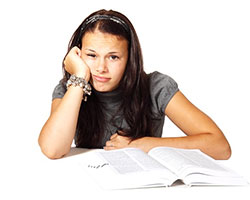 A bored-looking young woman facing the viewer, holding her head with one arm, an open book laid in front of her.