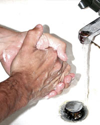 A pair of male hands rubbing together at a bathroom sink, next to a stream of water coming from a water tap, illustrating excessive hand washing.