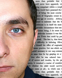 Half of a face, a young man with short, dark hair facing the viewer, with text on a whiteboard in the background.