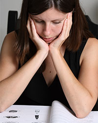 A young woman with dark hair facing the viewer is looking down at an open workbook, concentrating on the illustrations contained in the book.